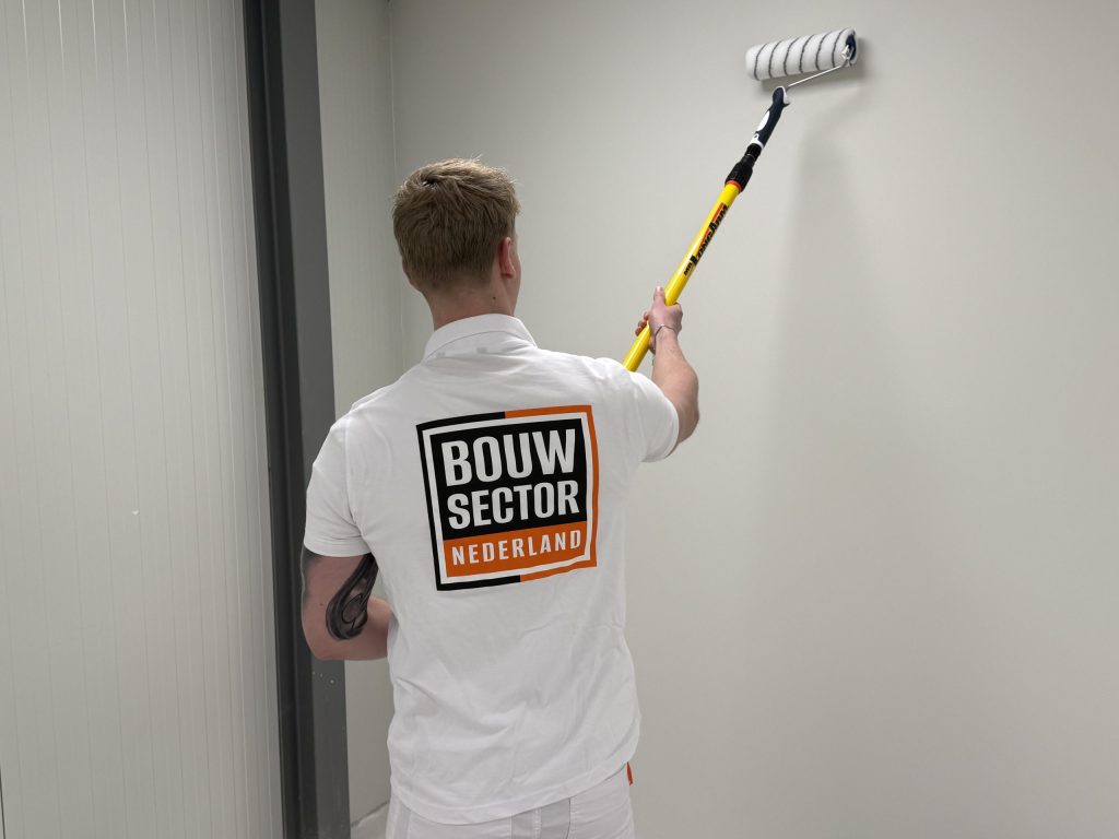 Schilder met het Bouwsector Nederland-logo op zijn rug rolt een witte wand met een lange verfroller